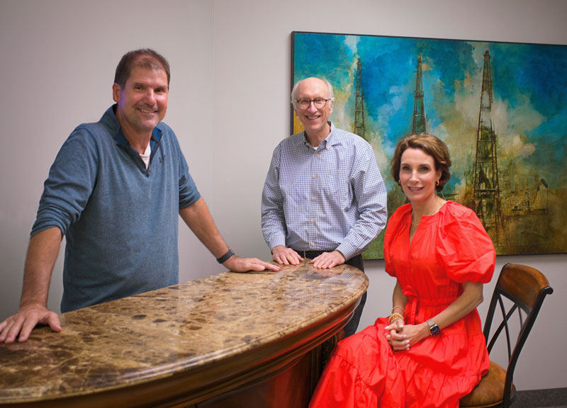 three members of case bogart Kit Bill and Cristin gathered at table with painting of three towers in the background dallas texas